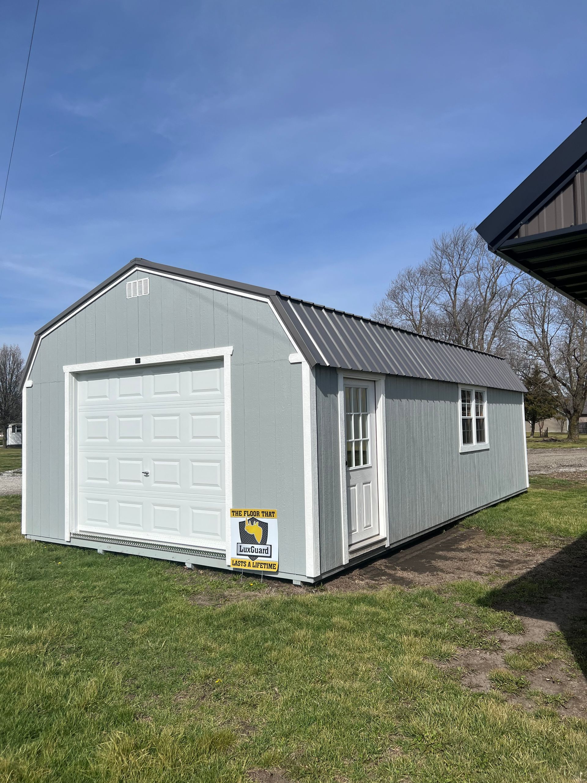 Gray shed with white garage door and snow-covered ground under a clear sky.