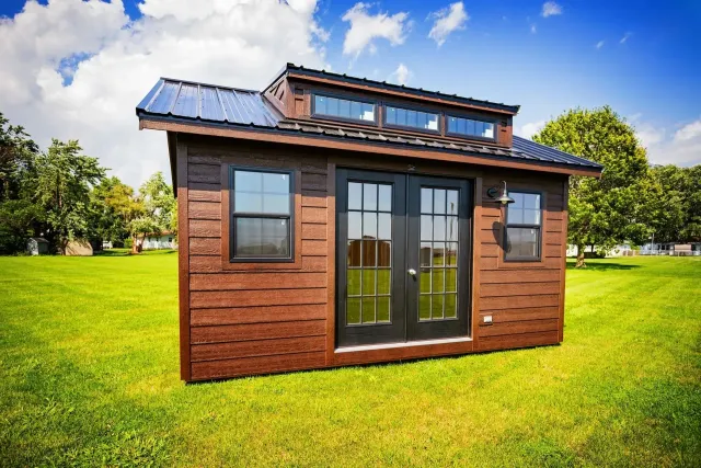 Brown tiny house with black door and windows on green grass under blue sky.