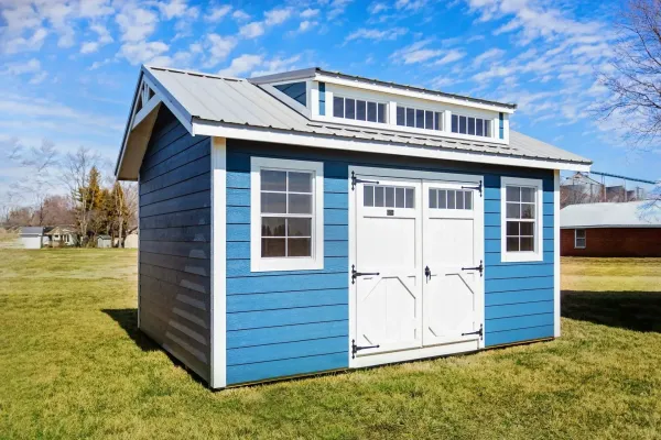 Blue shed with white trim and doors, metal roof, on grassy lawn.