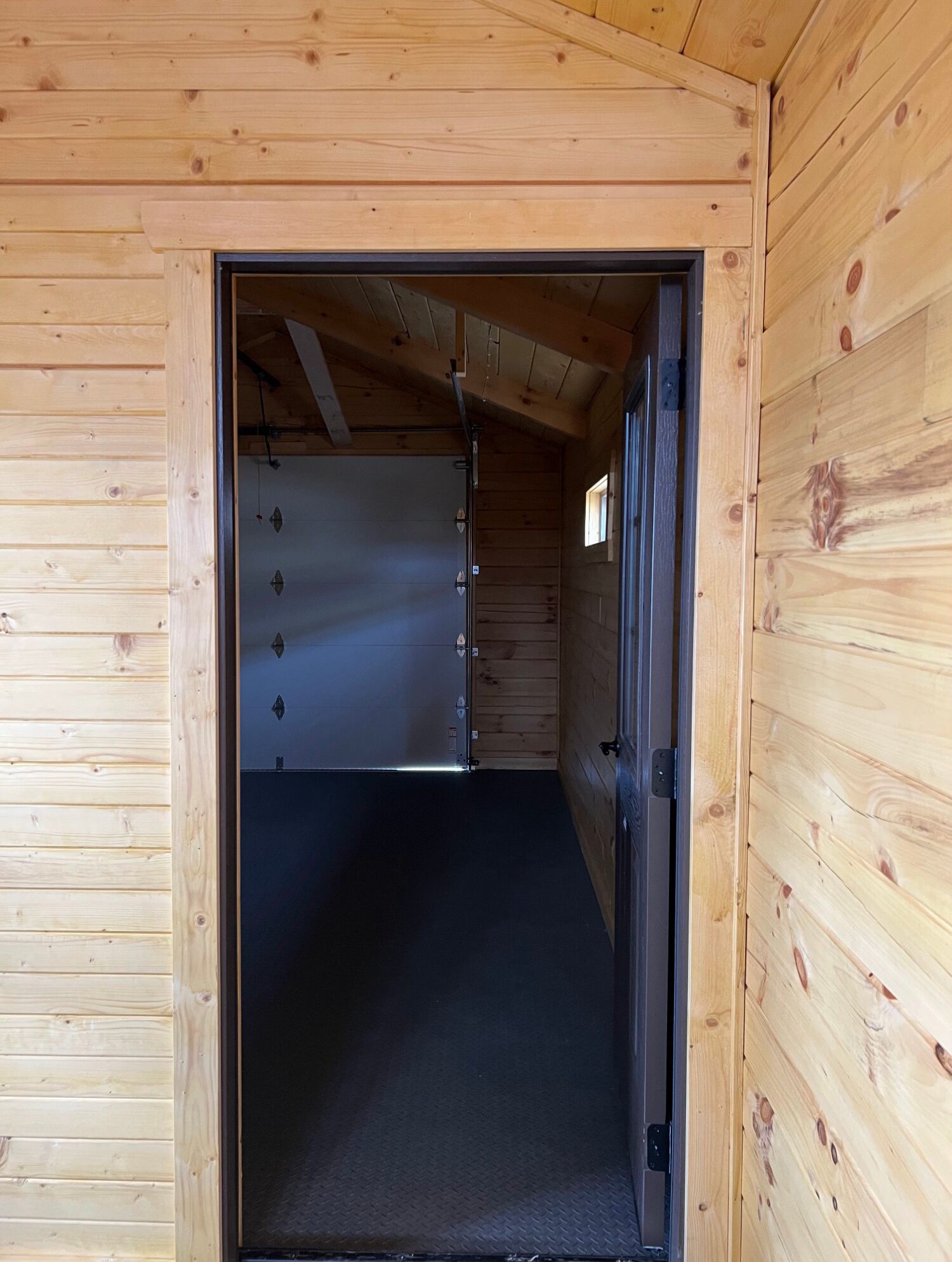 An open doorway framed in light wood leads into a dark, carpeted interior with visible wall paneling and a garage door.