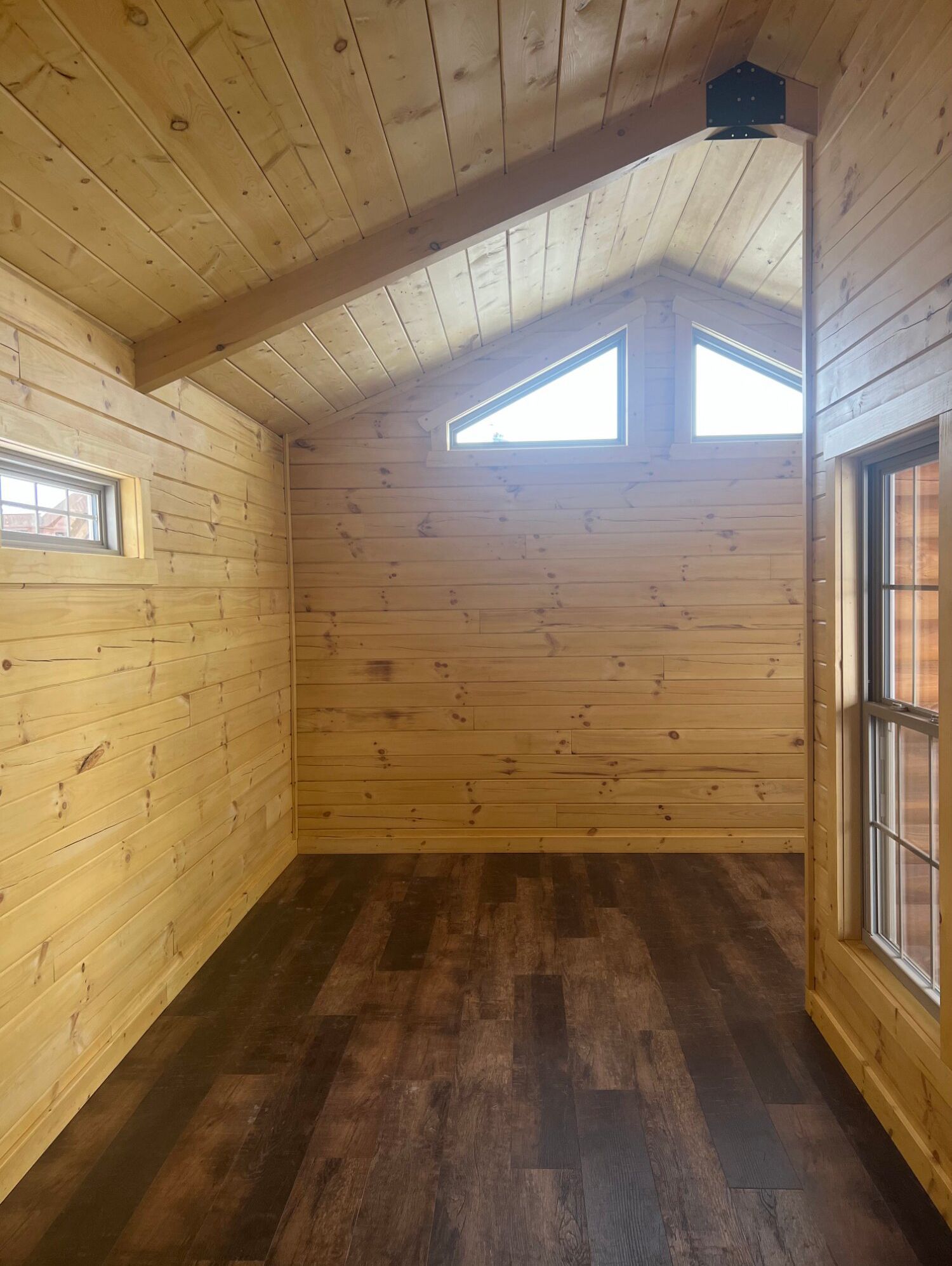 An interior view of a rustic wooden cabin room with vaulted ceilings, natural wood walls, and dark wood-look flooring.