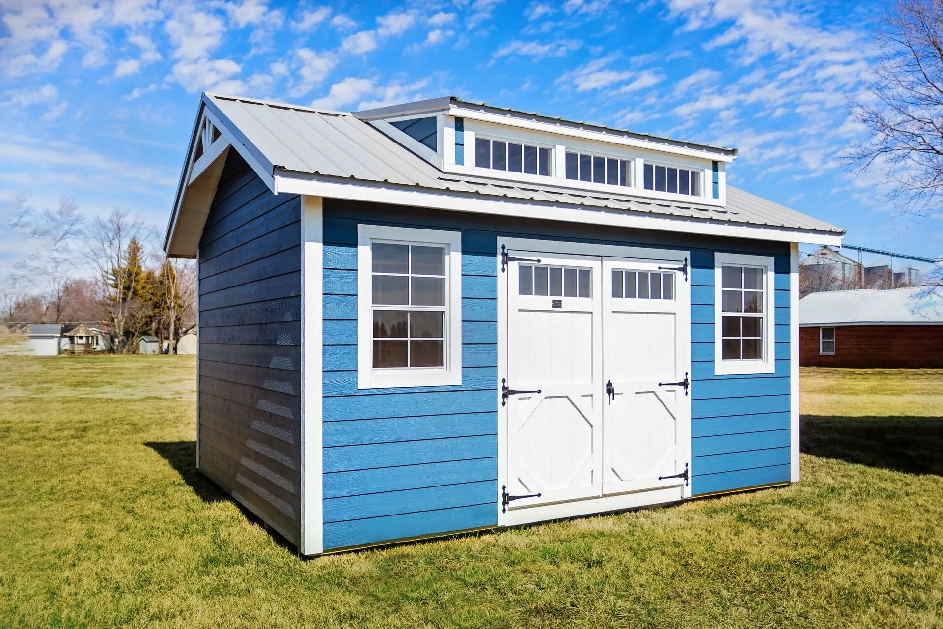 Lawn with a wooden shed, fence, and steps next to a brick house under a bright sun.