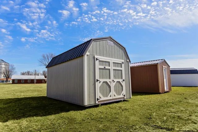 Grey gazebo on green grass, with a metal roof, near buildings.
