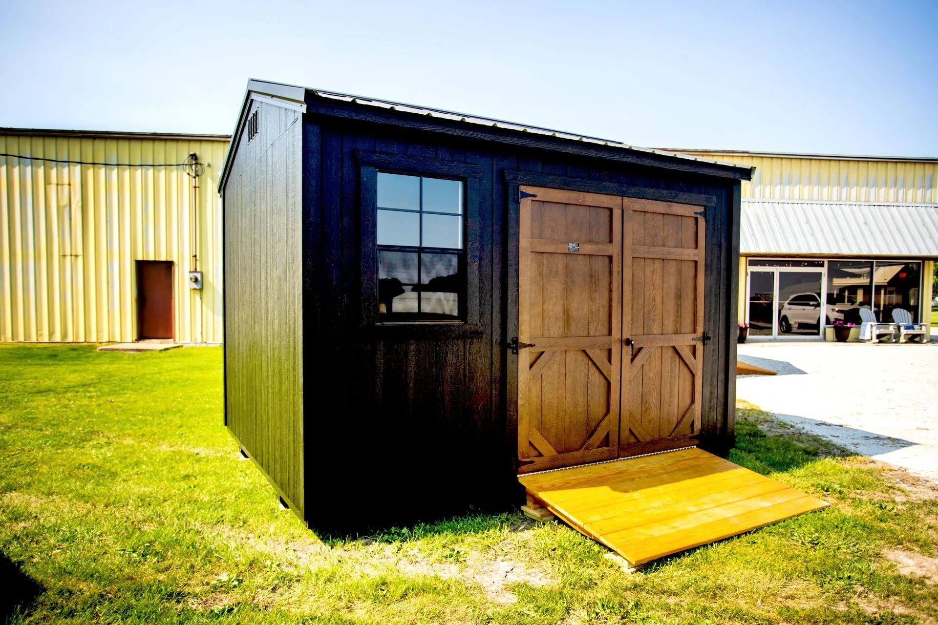 Black shed with brown doors and ramp, on green grass.