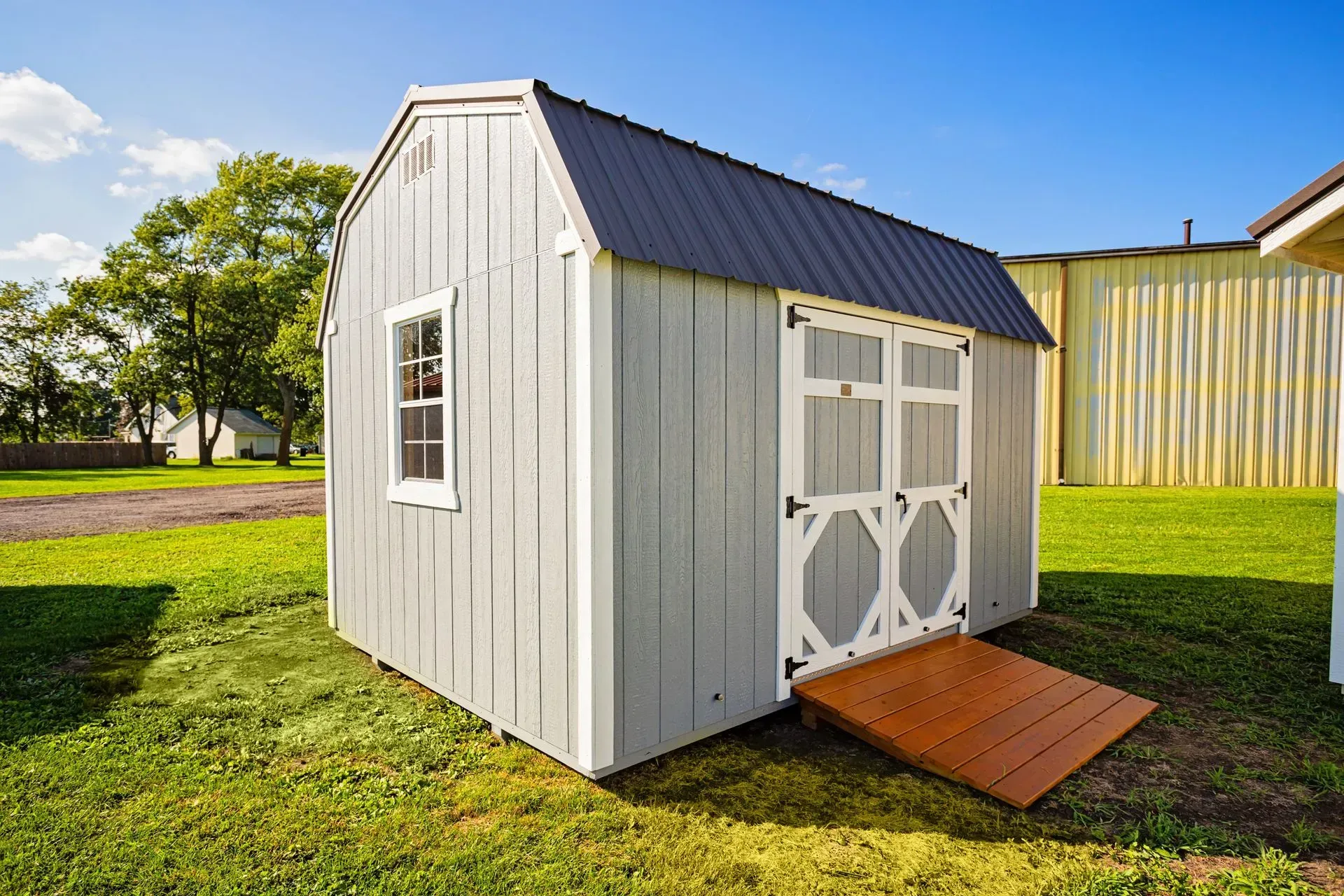 Gray storage shed with ramp and black roof on a green lawn.
