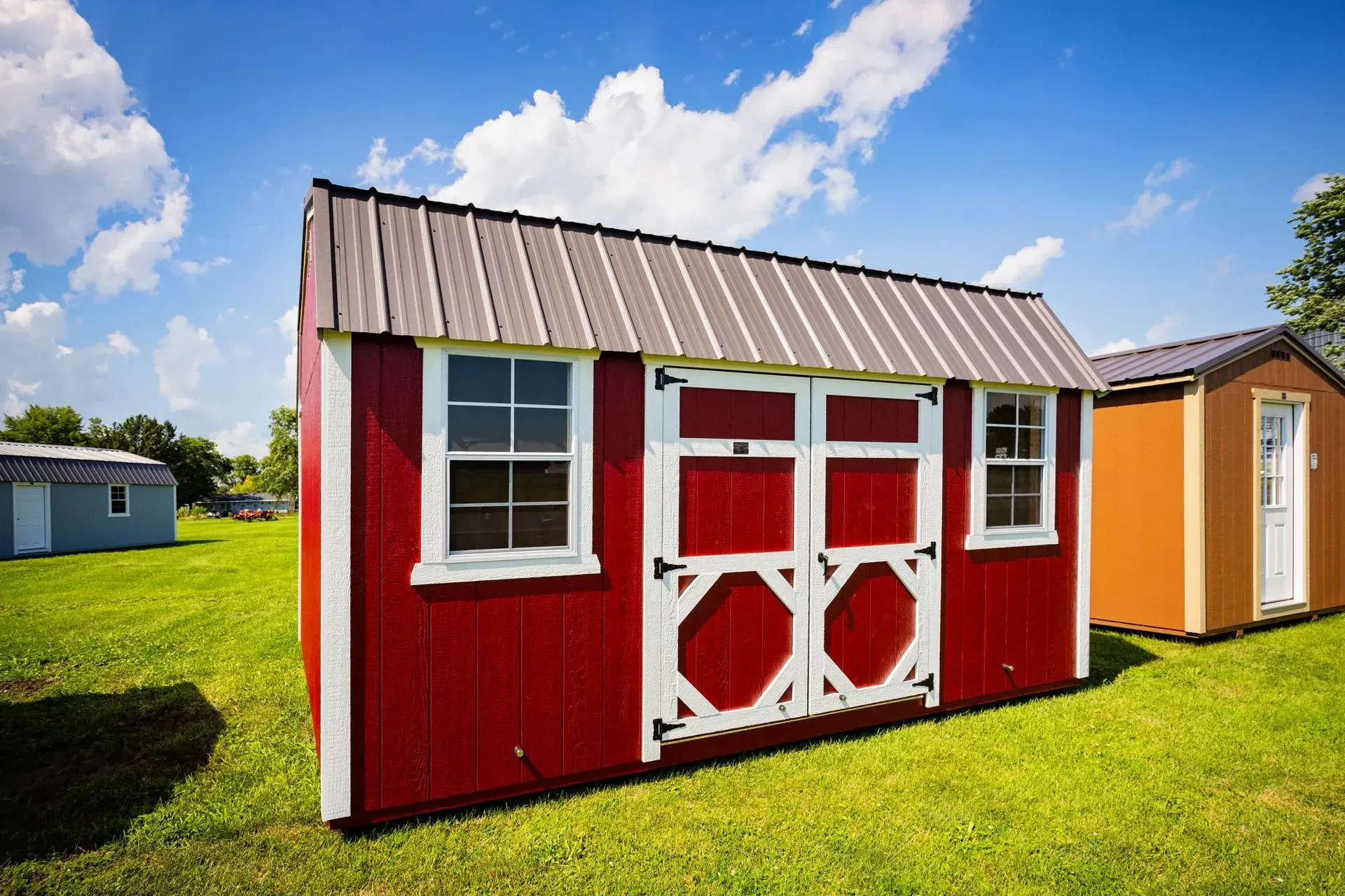 Red shed with white trim, brown metal roof, and double doors on a grassy lawn with blue sky.