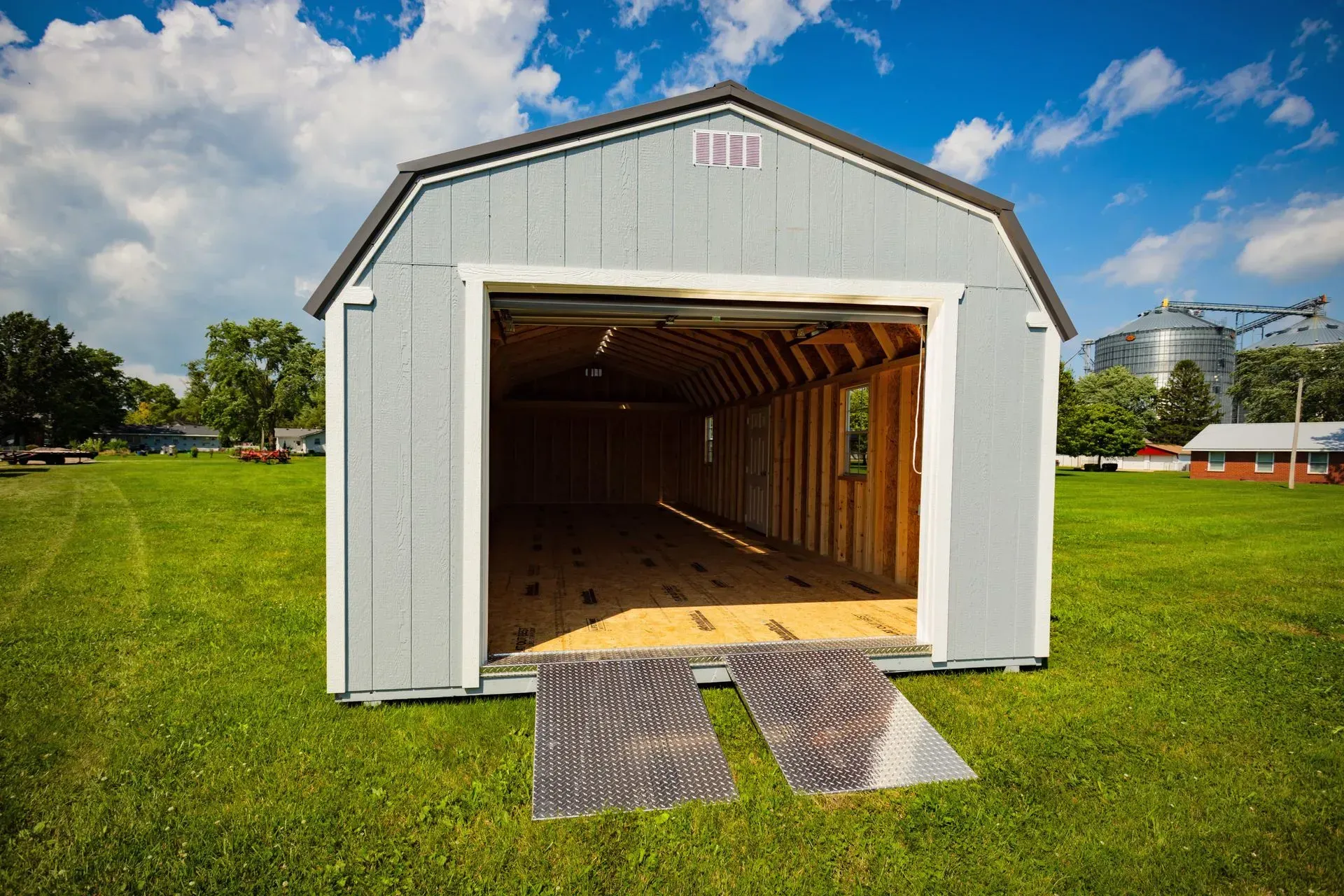 Gray shed with open door on a grassy field, two ramps in front.