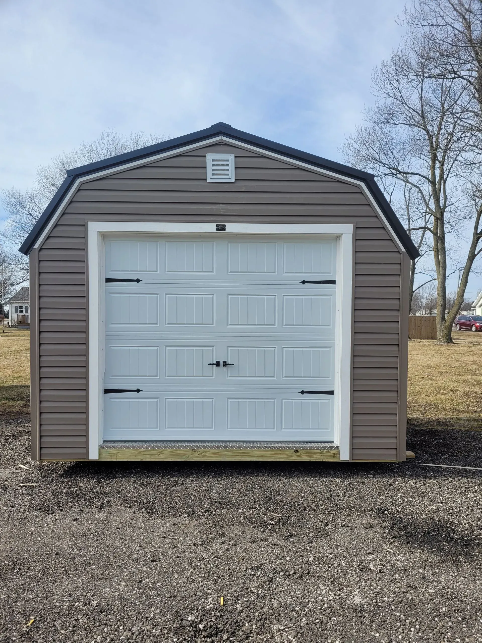 Tan storage shed with white garage door and black accents.