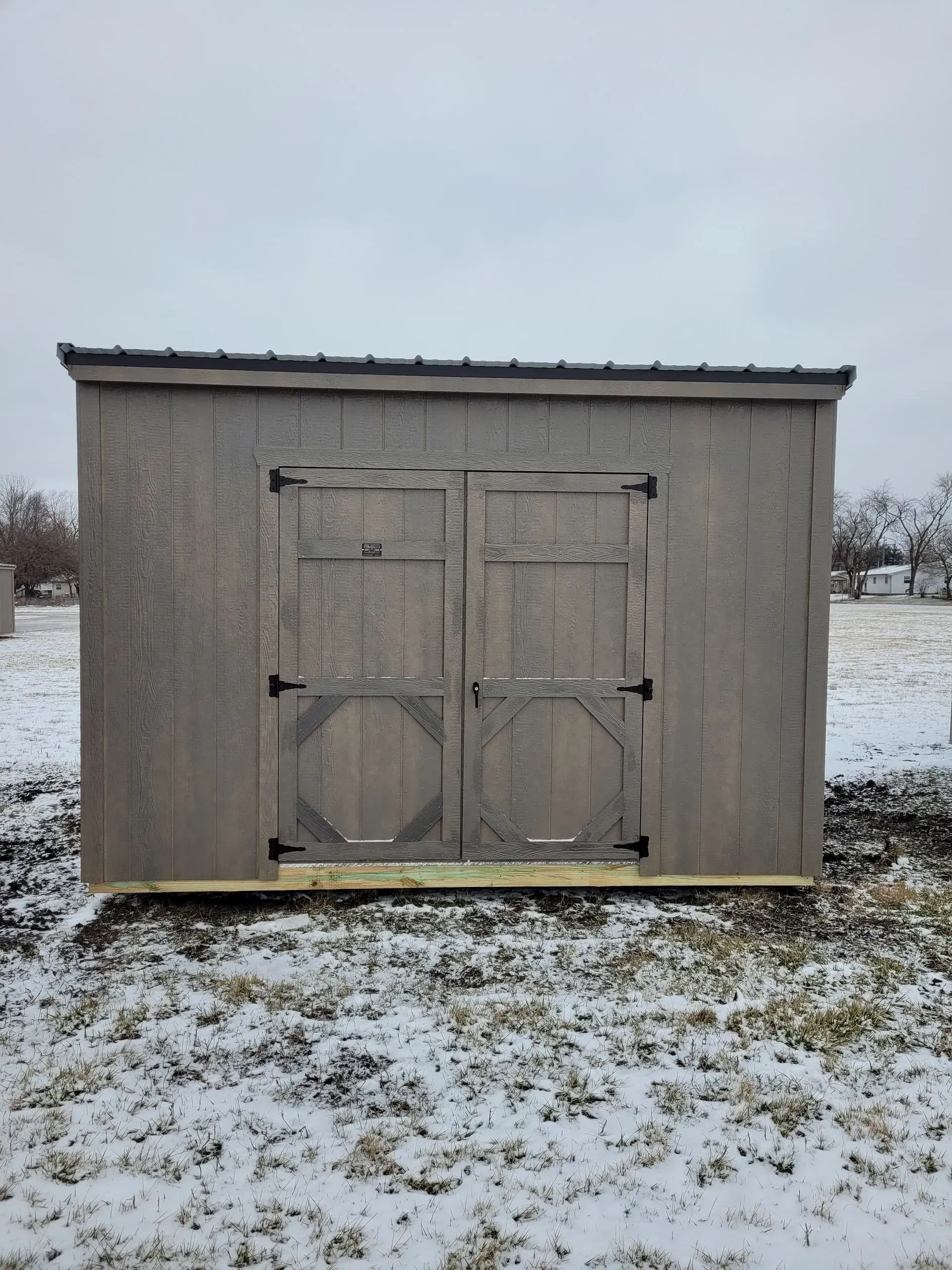 Gray wooden shed with double doors, set on snowy ground.