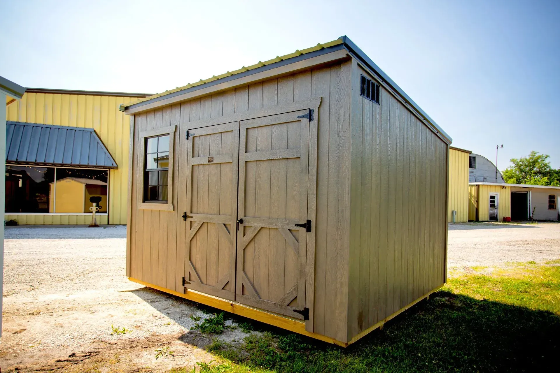 Tan shed with double doors and window on a sunny day.