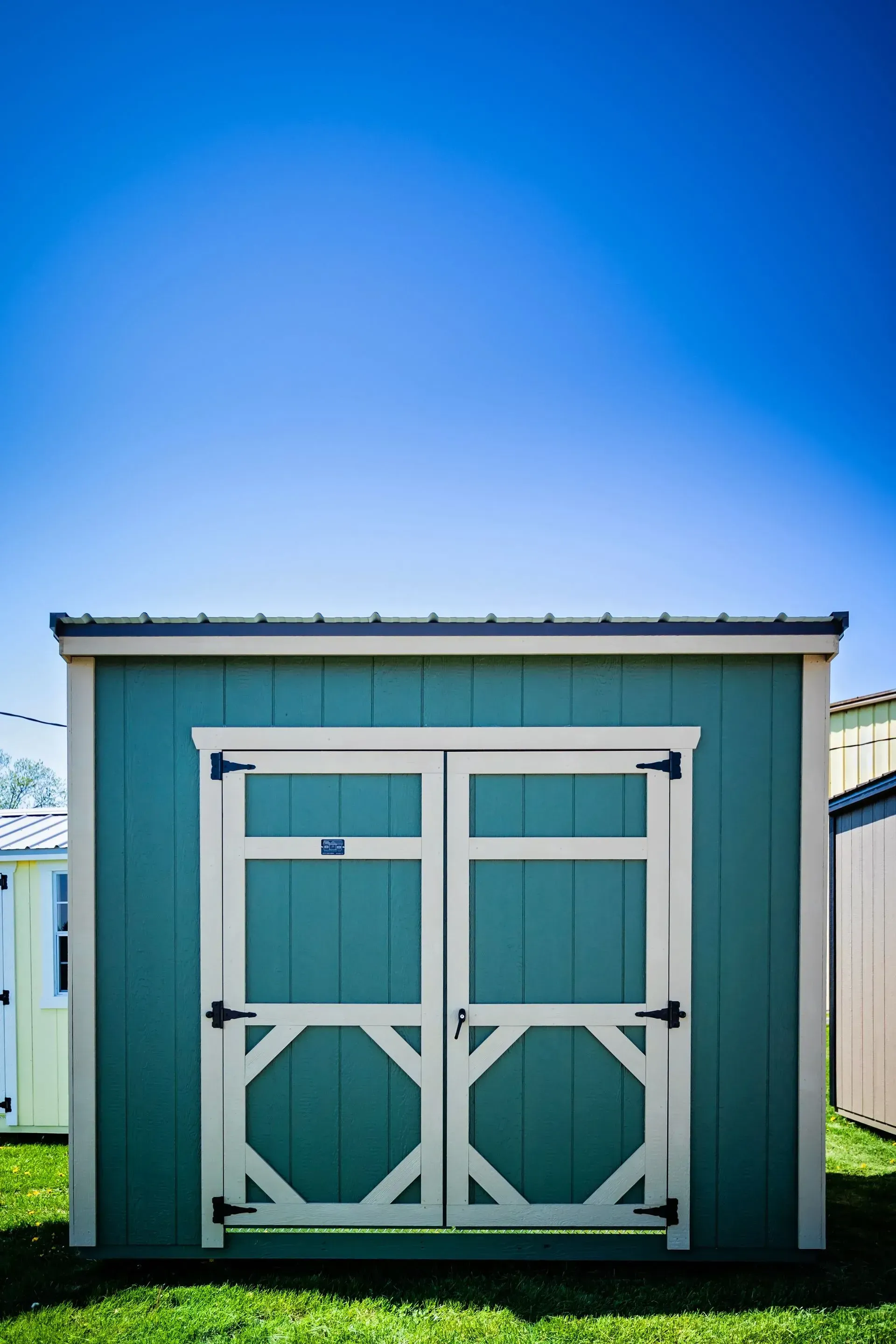 Teal storage shed with white trim and doors, set against a bright blue sky.