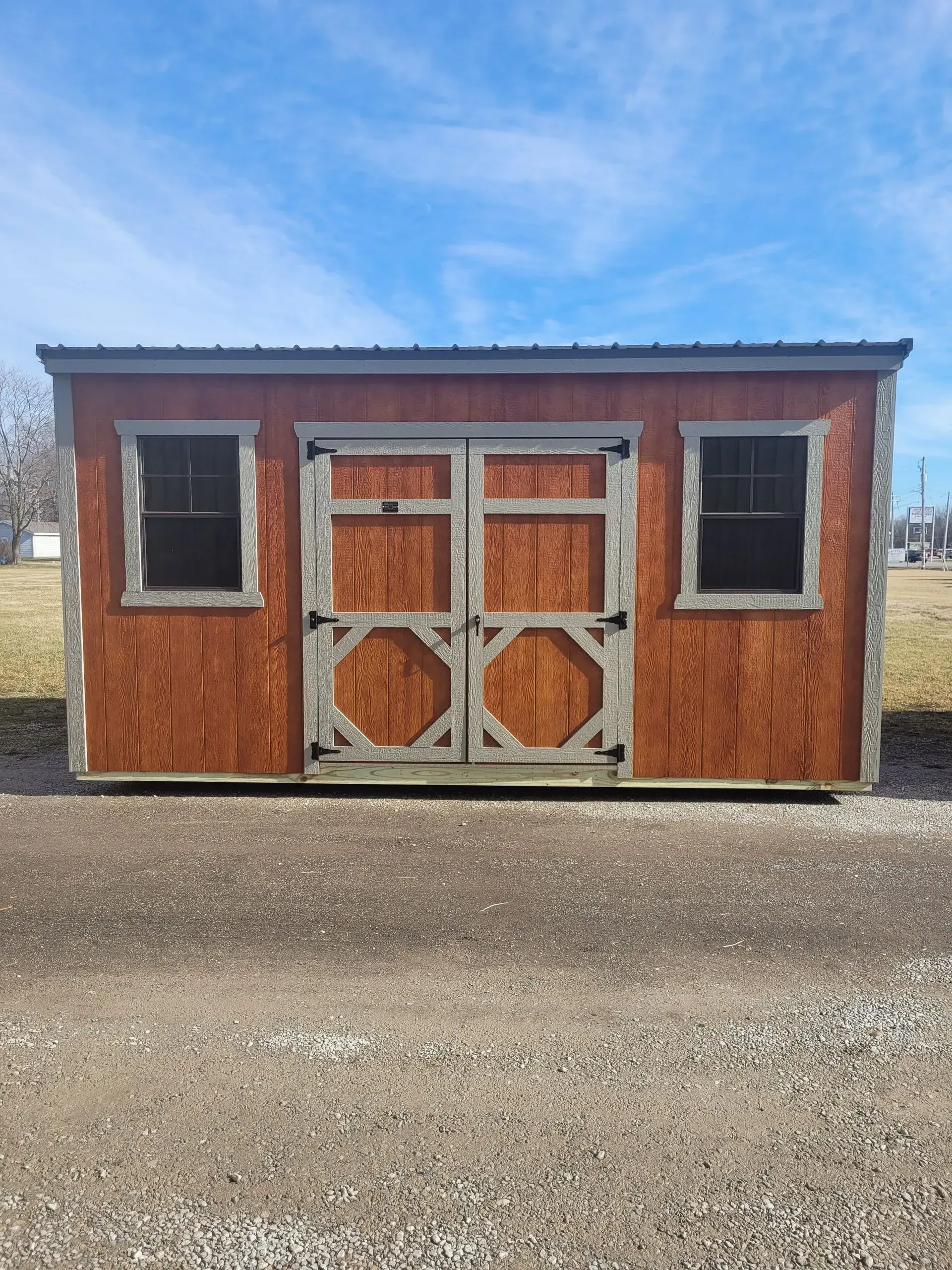 Brown wooden storage shed with double doors and two windows against a blue sky.