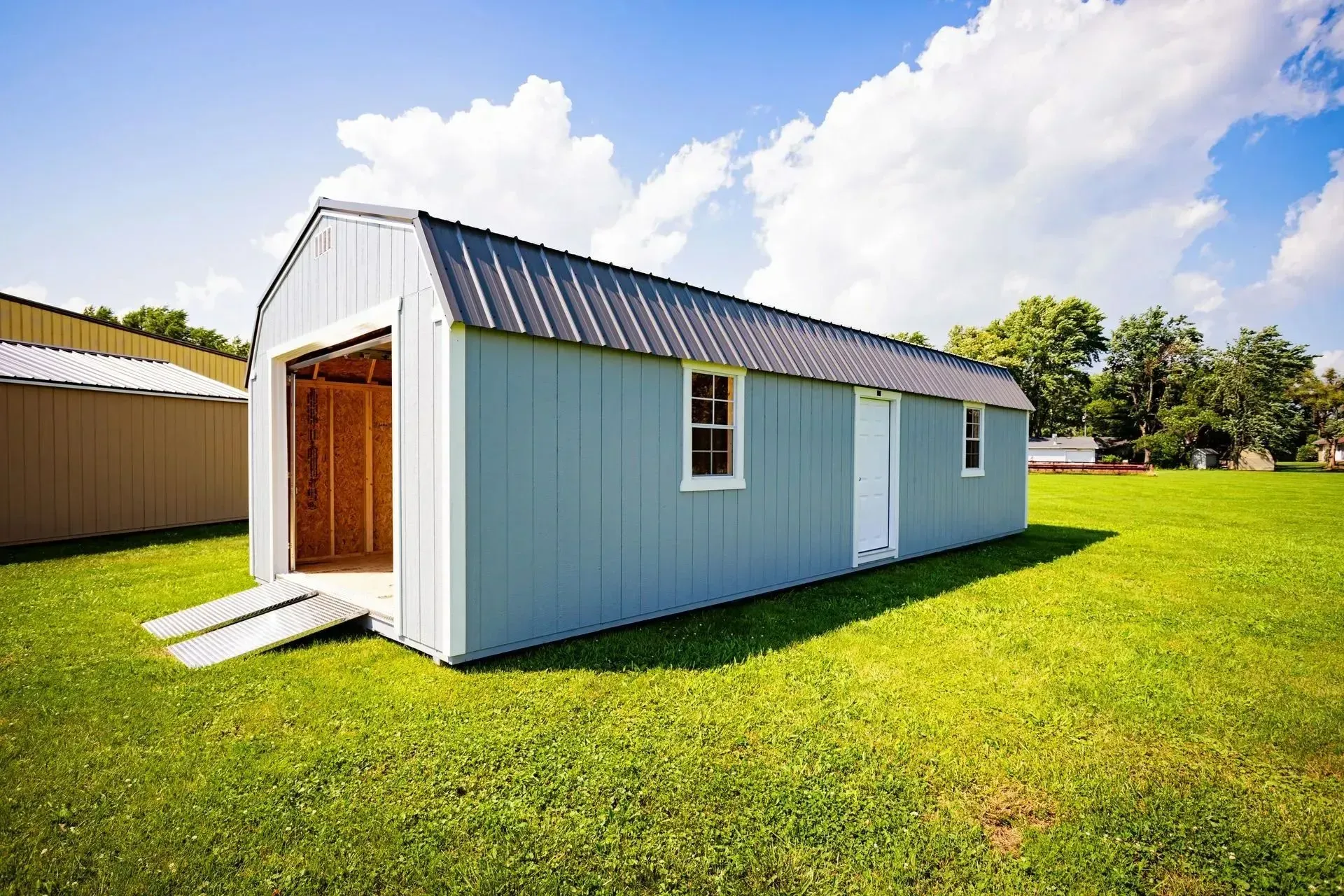 Blue shed with open garage door on green grass under a blue sky.