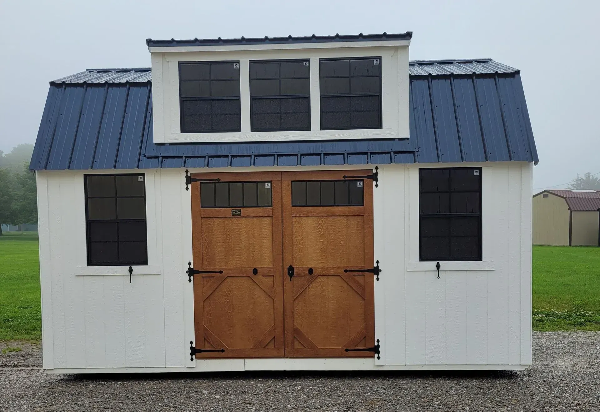 White shed with blue metal roof, brown double doors, and three windows above.