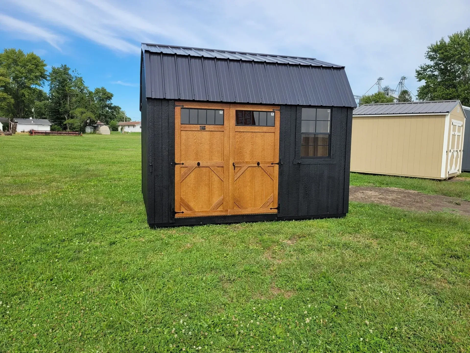Black shed with brown doors and a black metal roof on green grass.