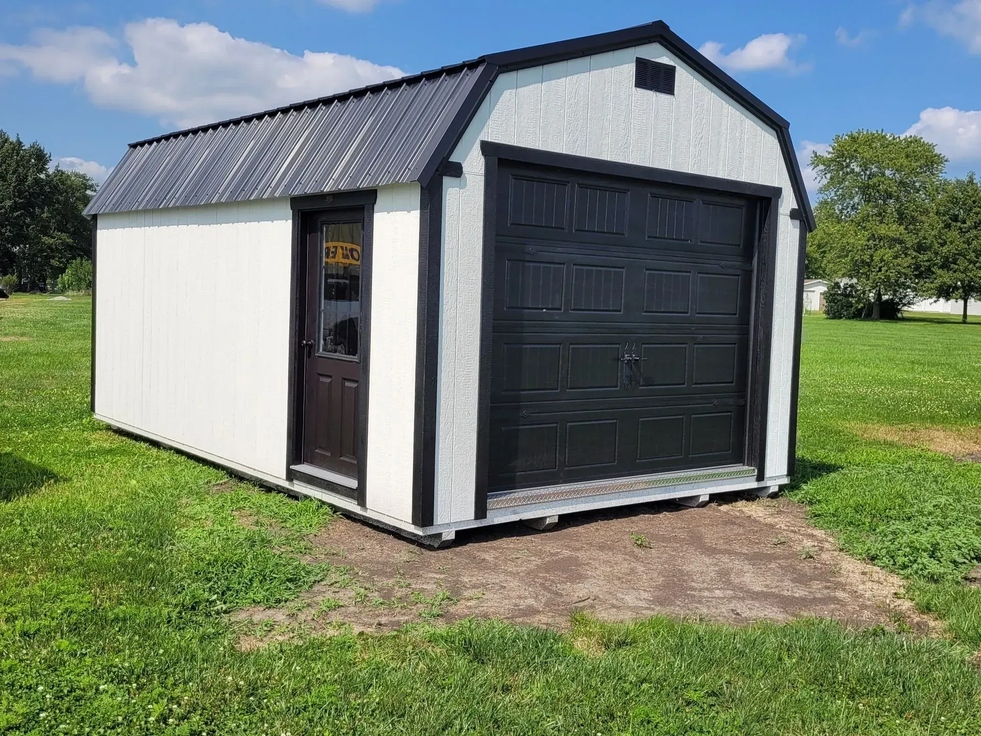 White shed with black trim, door, and garage door on a grassy field.