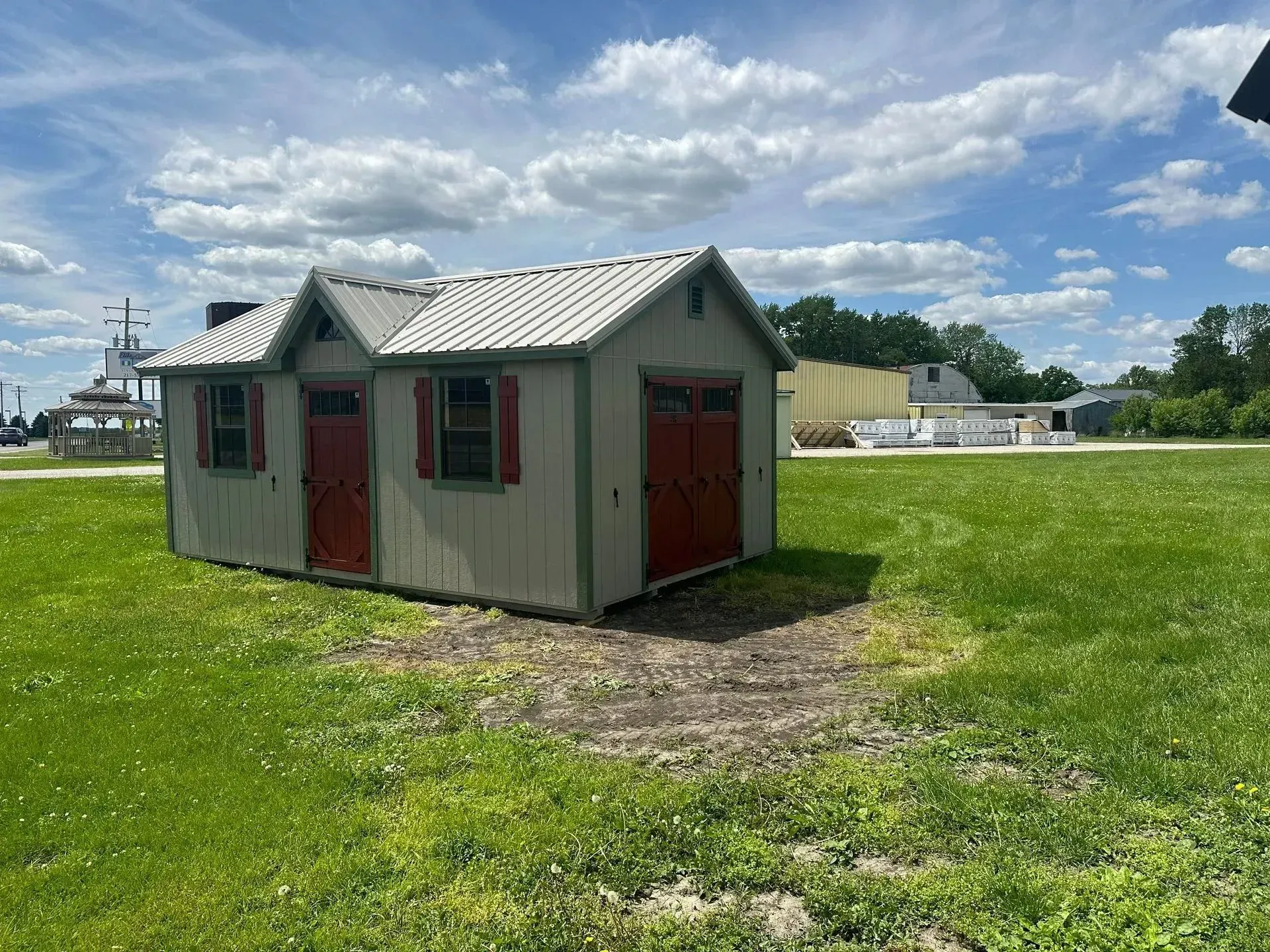 Small shed with red doors and shutters on a grassy field under a cloudy sky.