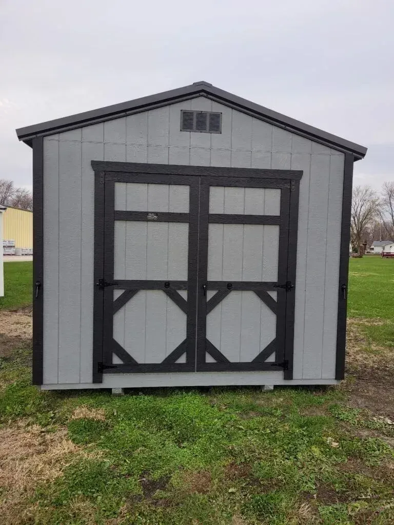 Gray storage shed with black trim and double doors on a grassy lot.