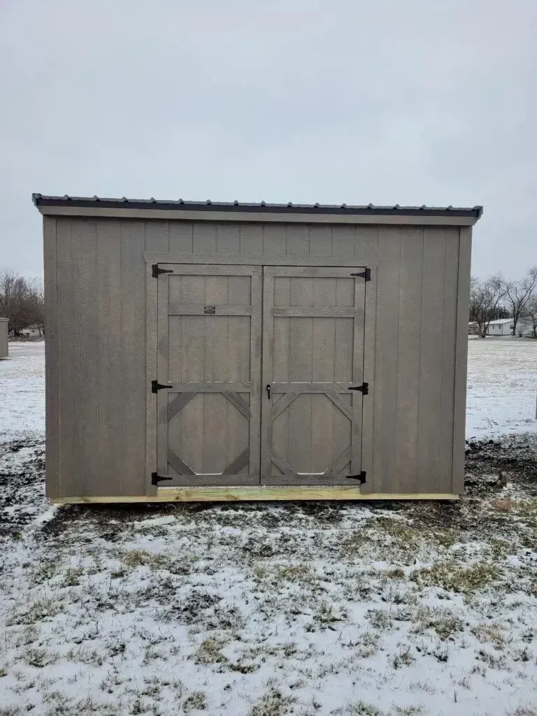 Gray wooden shed with double doors, set on a snowy field.