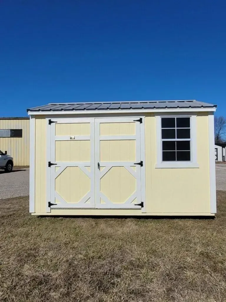 Yellow shed with white trim, black door hardware, window, and metal roof on a grassy plot.