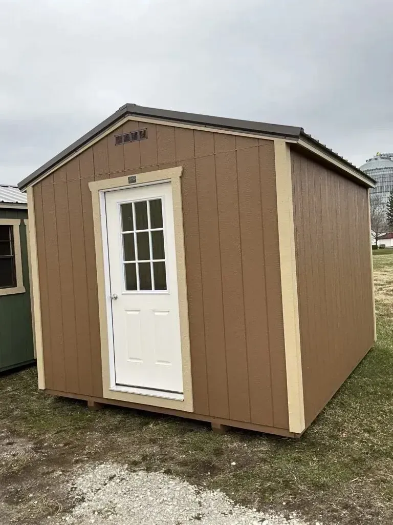 Brown shed with white door, beige trim, and a gray roof sits on grass.