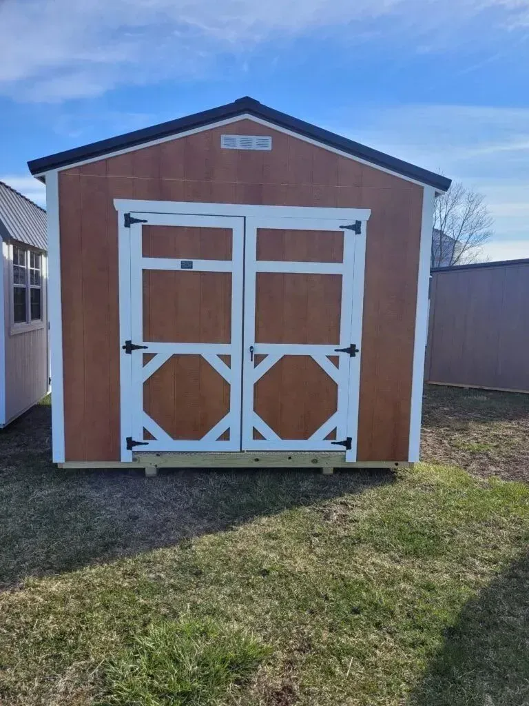Brown and white shed with double doors on green grass under a blue sky.