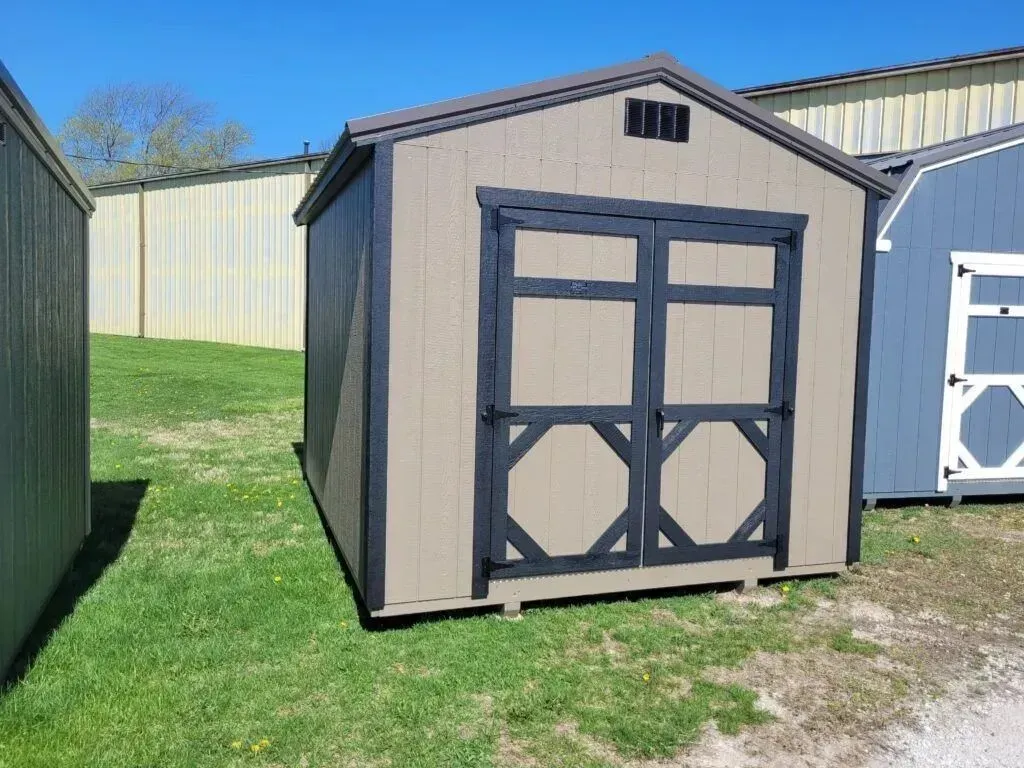 Tan shed with black trim and double doors on green grass.