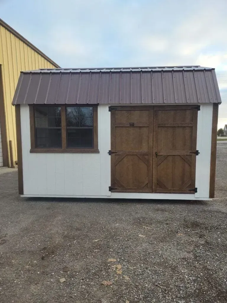 White and brown shed with brown roof, window, and double doors.