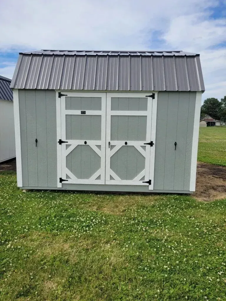 Gray shed with white trim, black door hardware, and metal roof, in grassy yard.