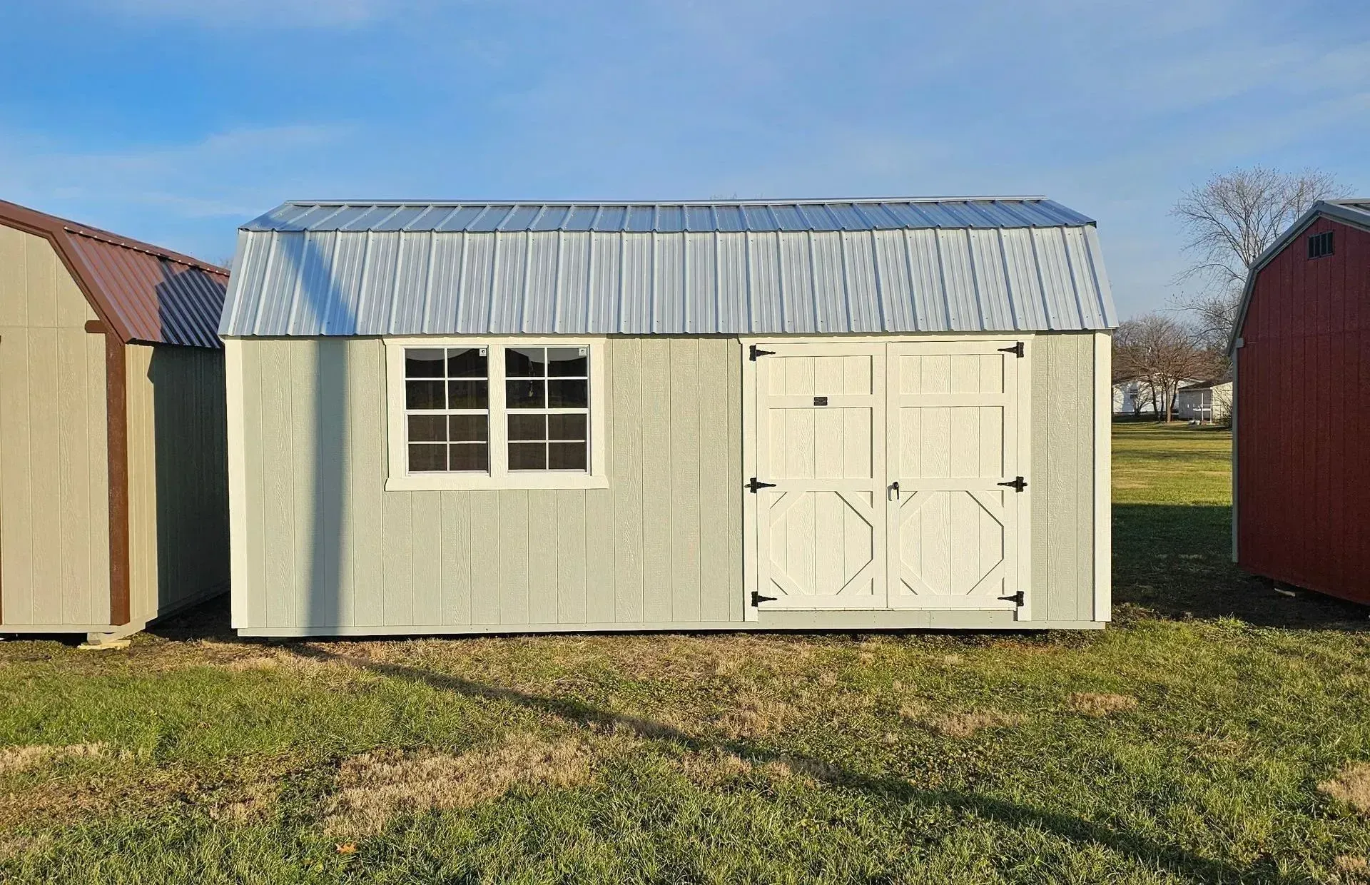 Light gray shed with white doors and window, metal roof, on grassy lot.