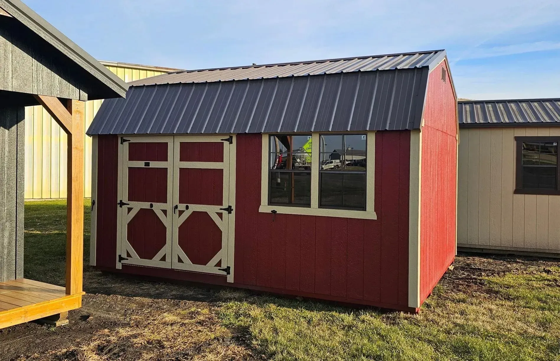 Red shed with a dark gray metal roof, cream trim, and double doors, next to other sheds.