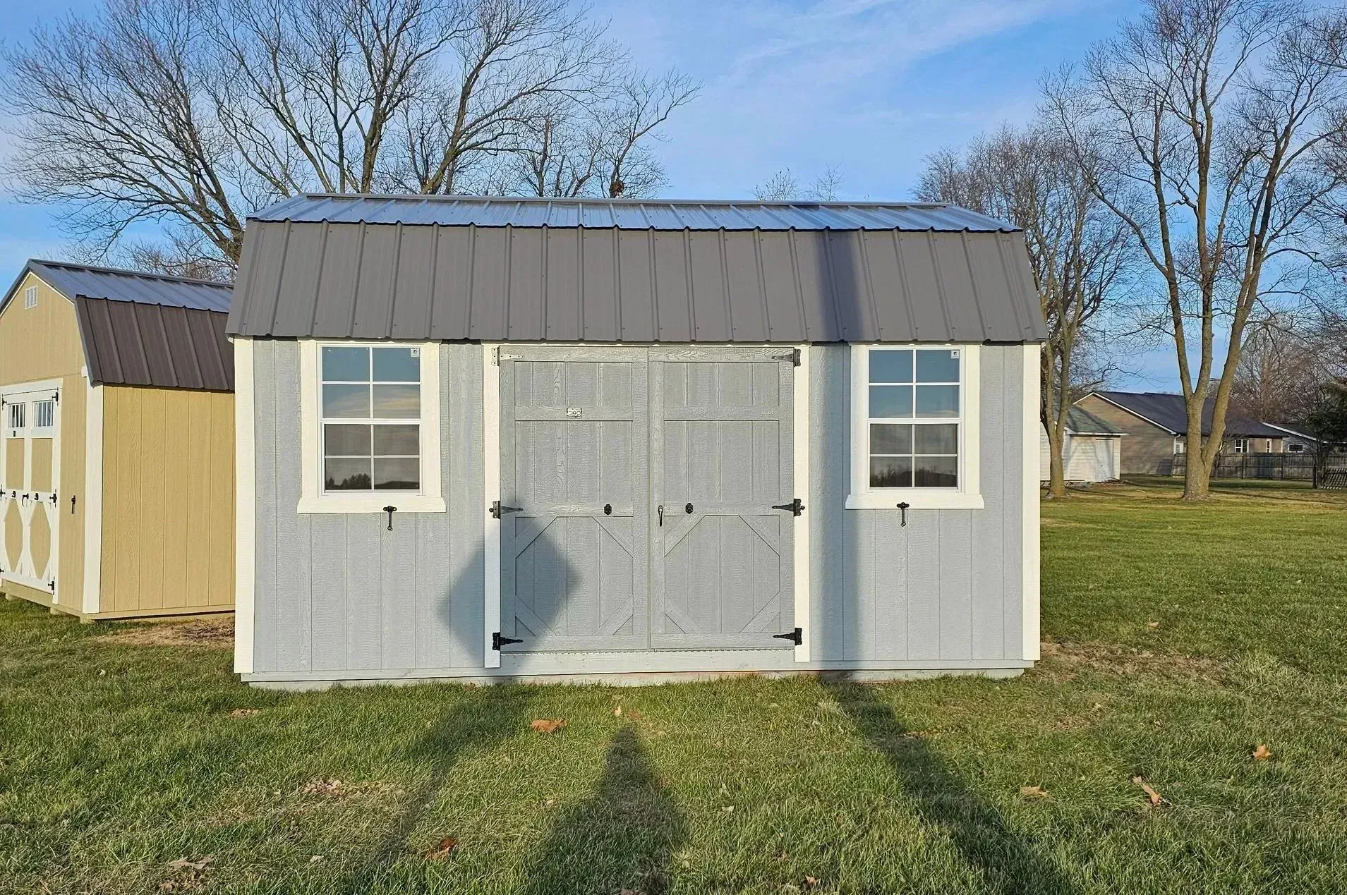 Light blue shed with gray roof, white trim, and double doors, in a grassy yard.