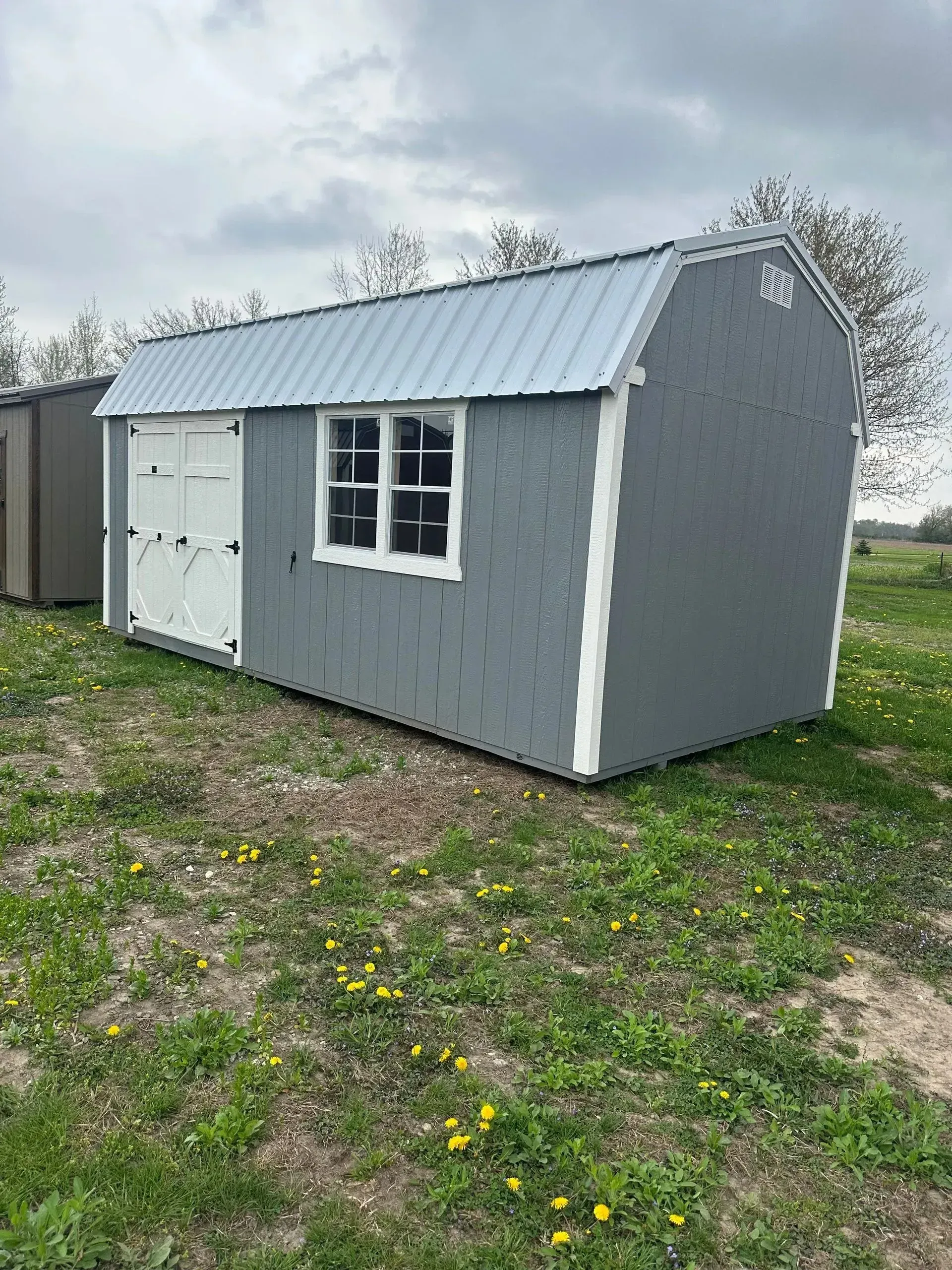Gray shed with white trim, door, and window; metal roof; set in grassy area.