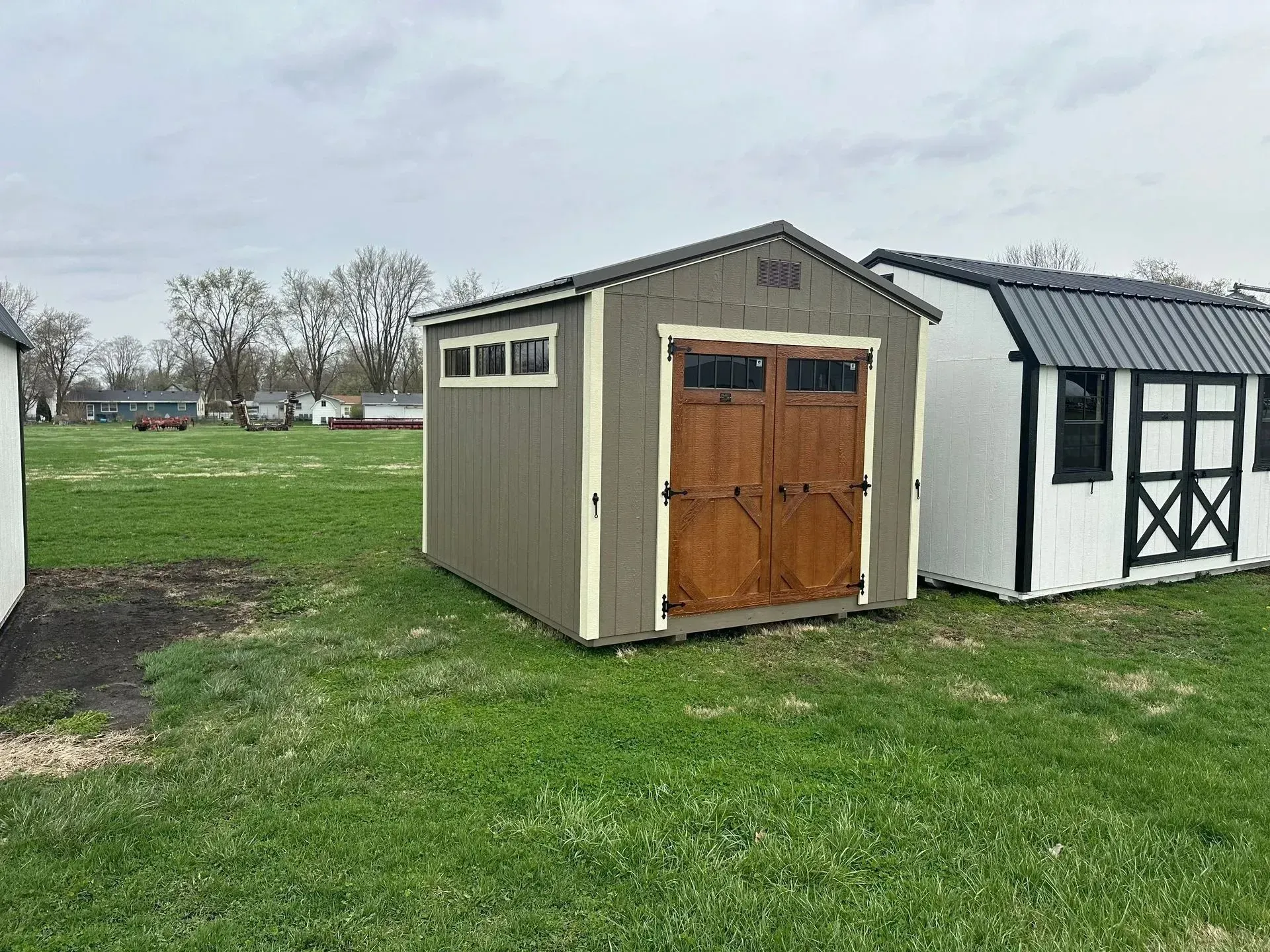 Brown and tan shed with wooden double doors, sitting on green grass.