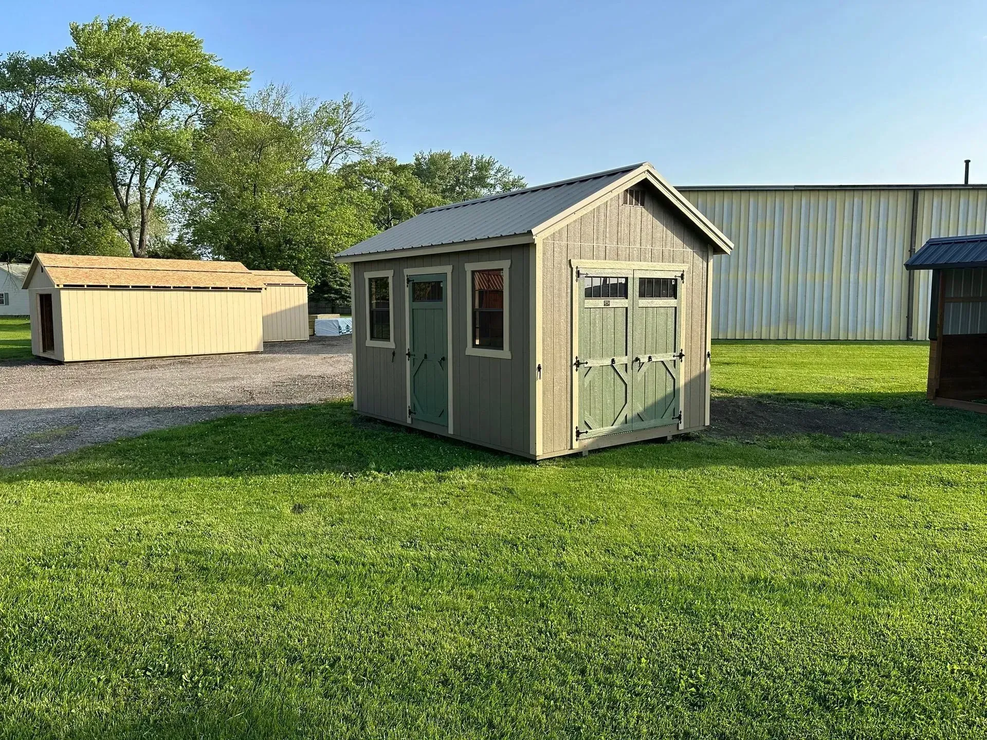 Green and gray storage shed on a grassy lot, with other sheds in the background.