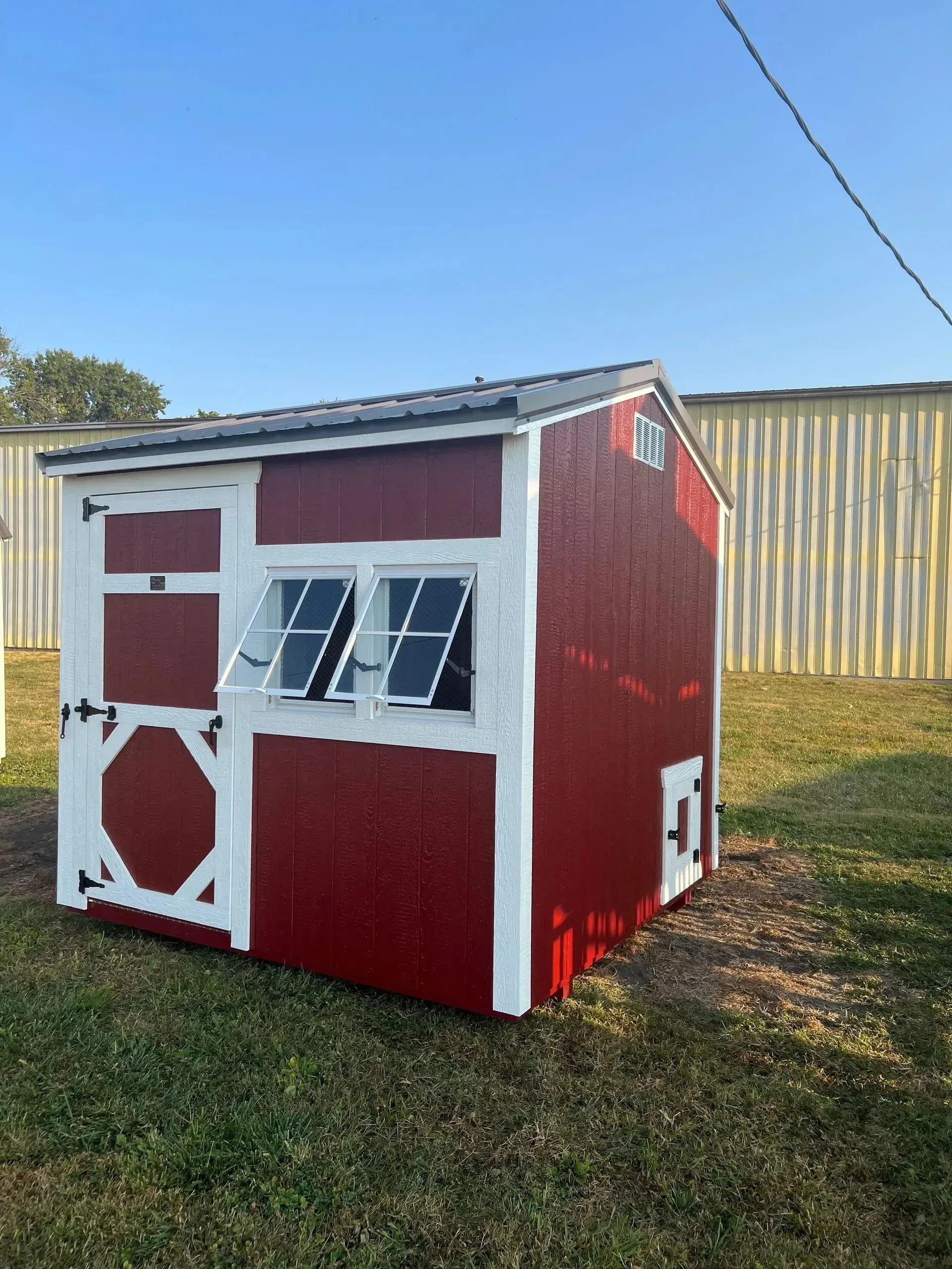 Red and white painted chicken coop on green grass, with two windows and a small door.