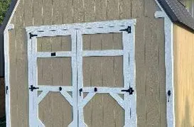 Tan shed with white-trimmed double doors and black hardware.