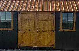 Dark shed with brown wooden double doors, copper roof, two windows.