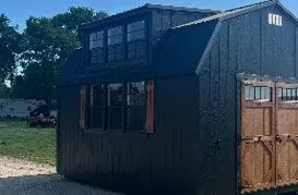 Black tiny house with brown garage doors and windows, set in a grassy yard.