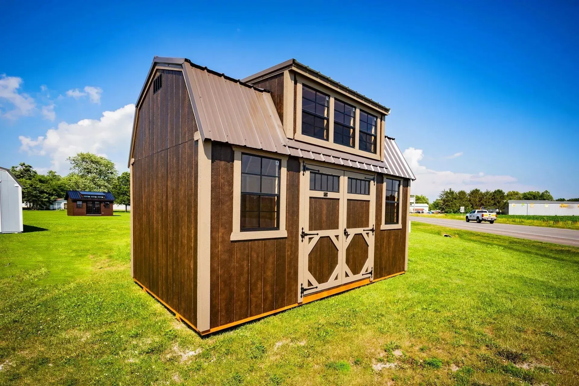 Brown shed with loft and metal roof, standing on grass under a blue sky.