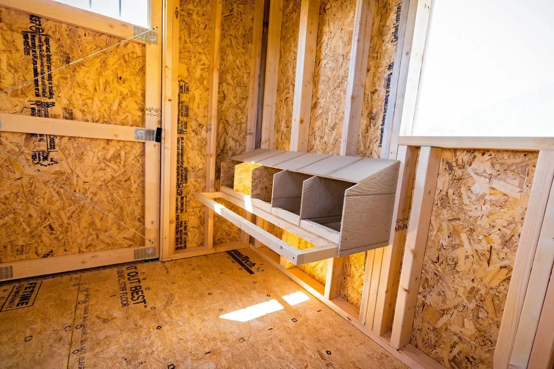 Interior view of a wooden chicken coop under construction, with a nesting box installed.
