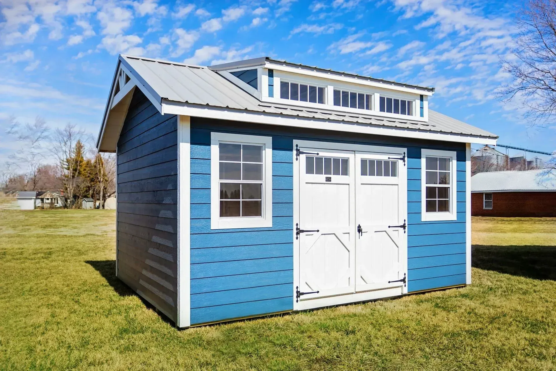 Blue storage shed with white trim, double doors, and clerestory windows, set on grass.