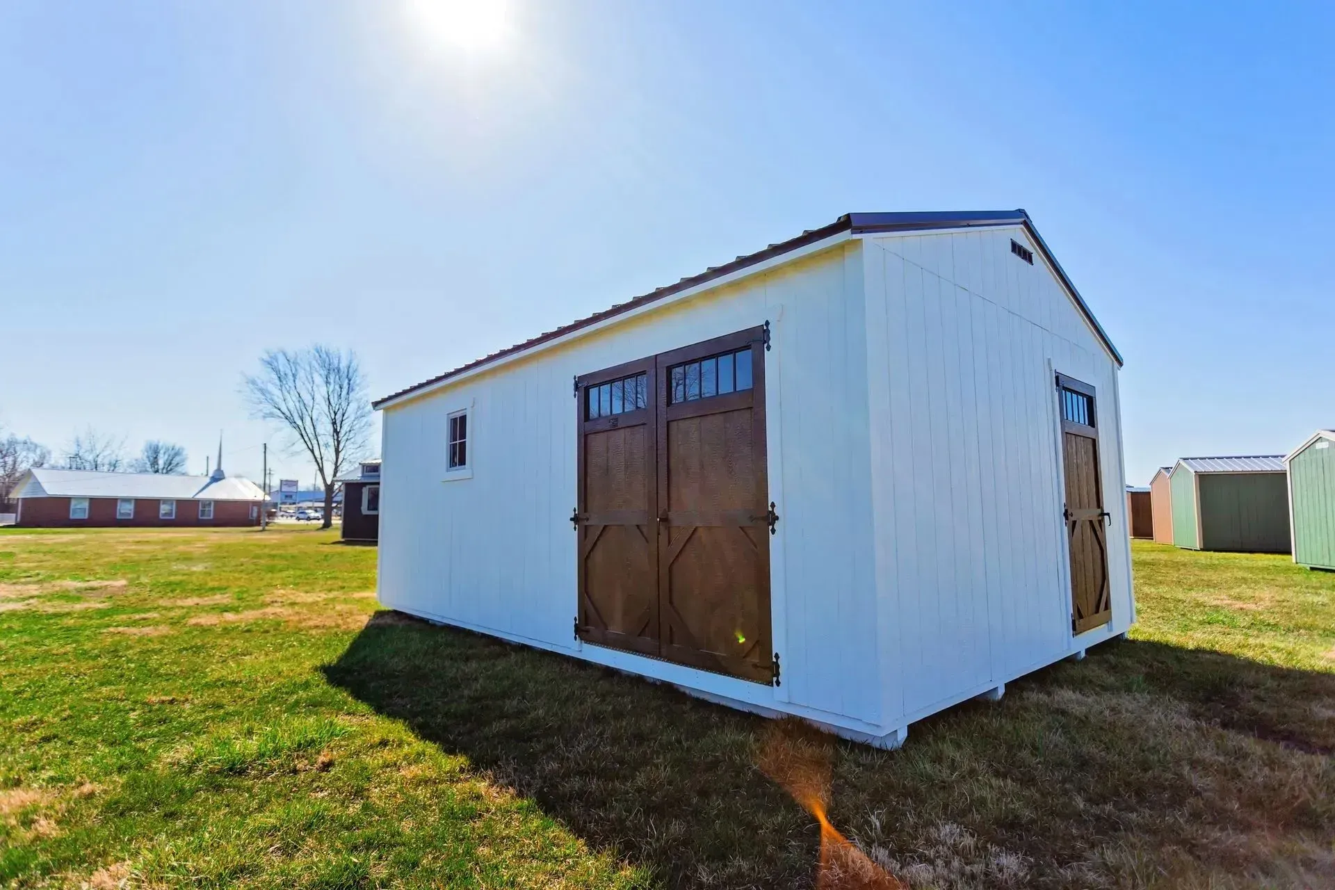 White shed with brown double doors, window, on green grass, sunny day.
