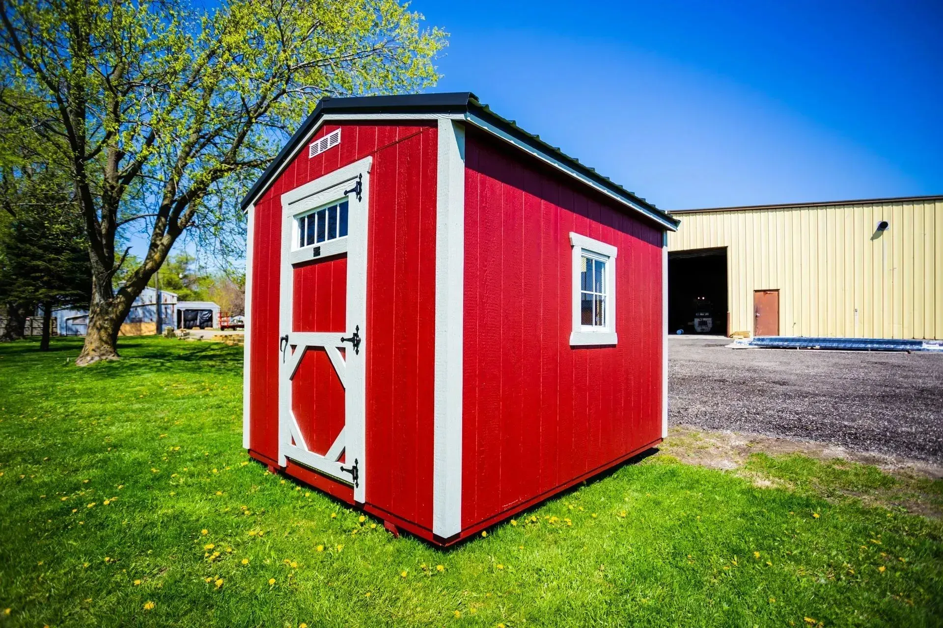 Red shed with white trim, a small window, and a door, on a grassy lawn.