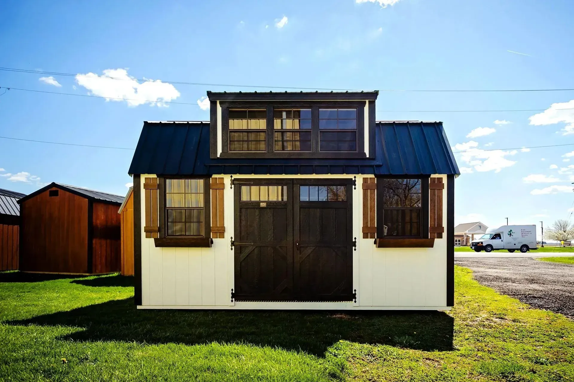 White and brown storage shed with a dark blue roof, on green grass under a blue sky.