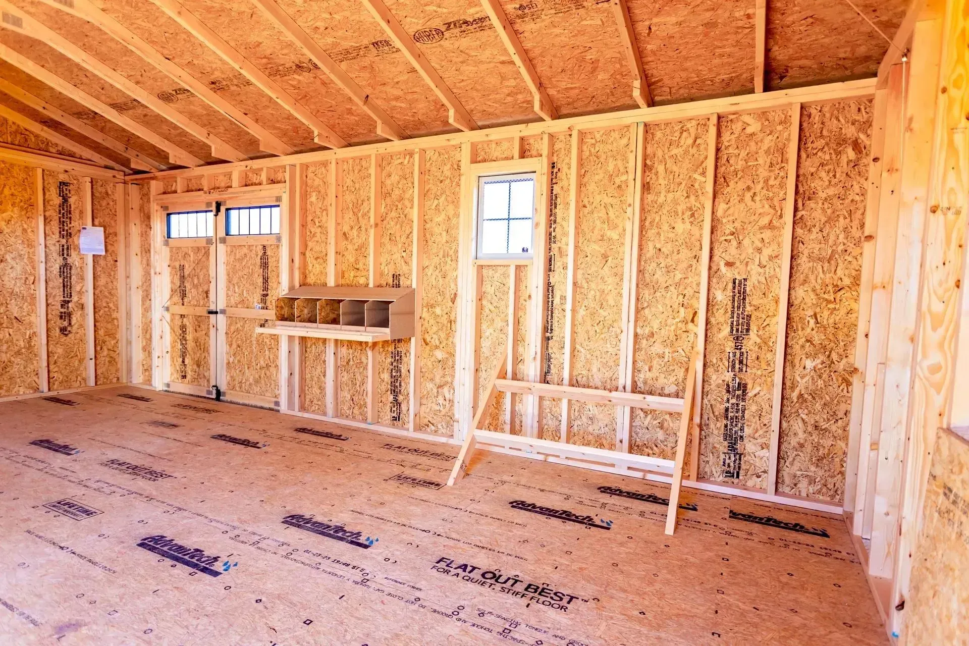 Interior of a wooden shed under construction with two windows, a nesting box, and a floor of oriented strand board.