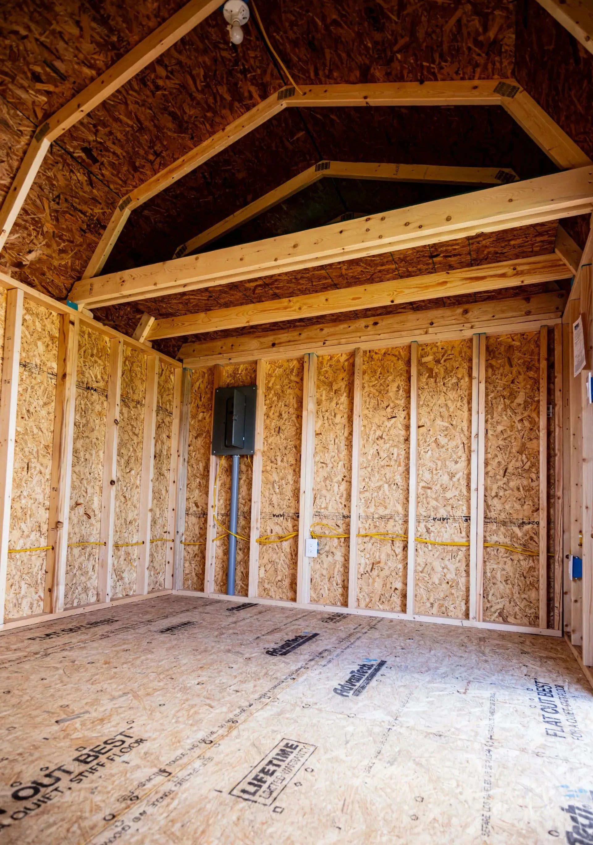 Interior of a wooden shed under construction, showing framing, flooring, and electrical components.
