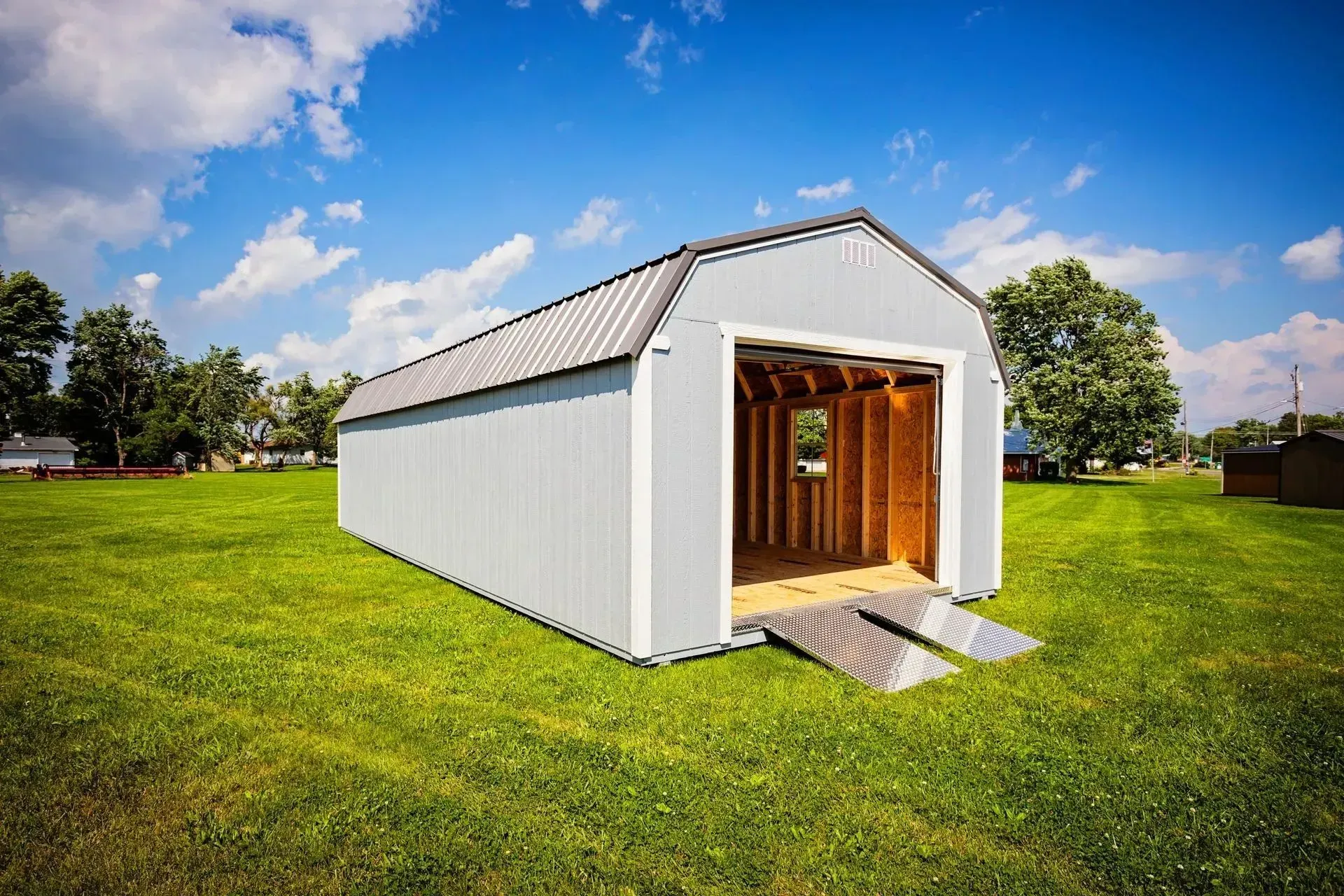 Light blue shed with open door and ramps on green grass under blue sky.