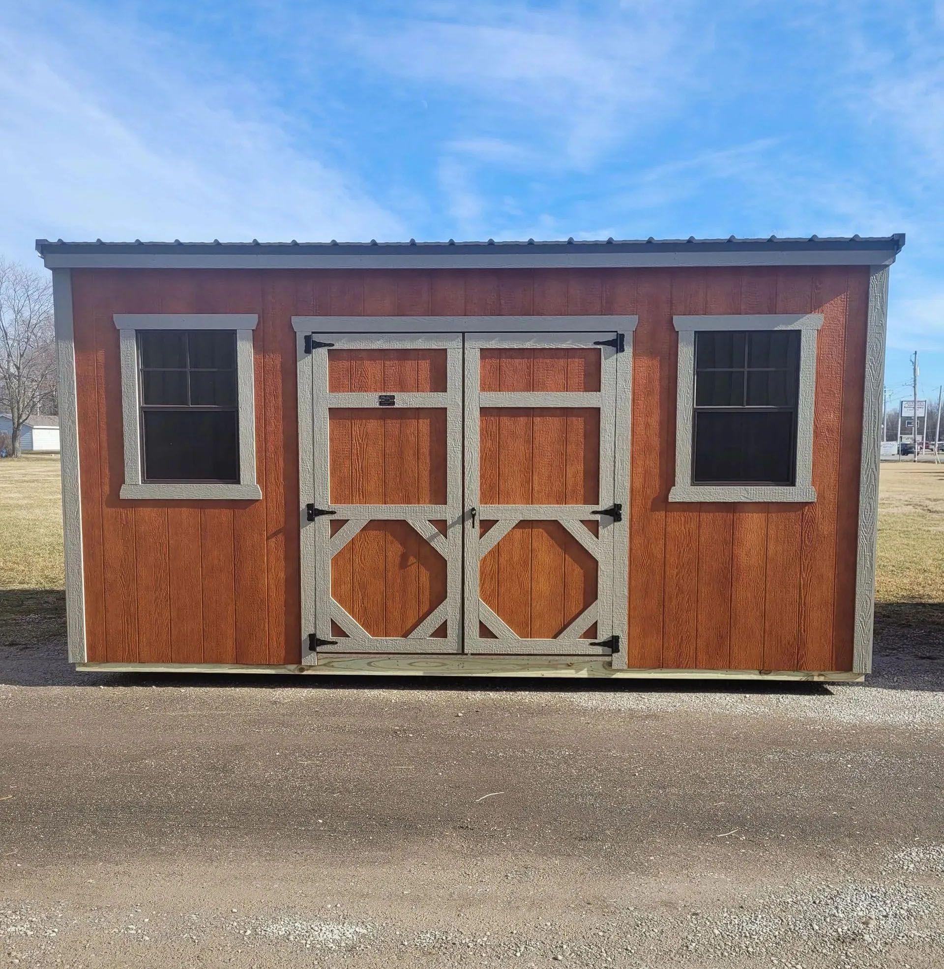 Red shed with gray trim, double doors, two windows, set in a field.