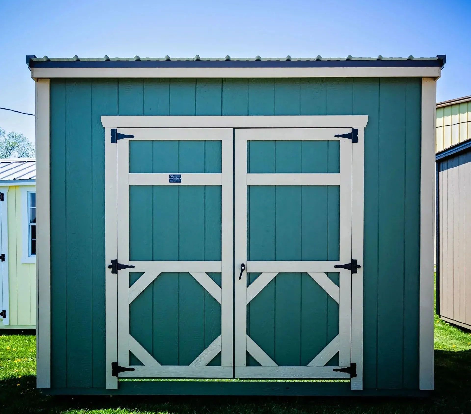 Green shed with tan trim and double doors. Black hardware.